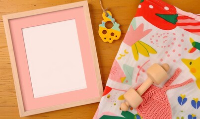 Wall Mural - A blank picture frame and colorful baby blanket on a wooden surf