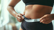 © Maksym - Closeup view of a woman's fat belly as she uses a measuring tape to measure the circumference, the tape snugly fitting around her waist