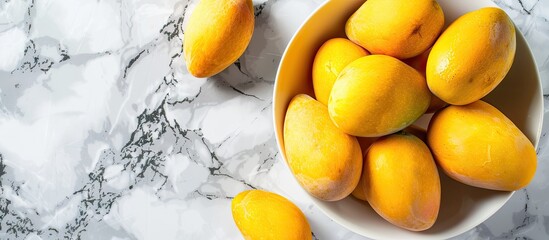 Canvas Print - A close up top view of ripe yellow mango fruits on a white bowl placed on a marble table creates a tropical summer ambiance with a flat lay composition featuring copy space image