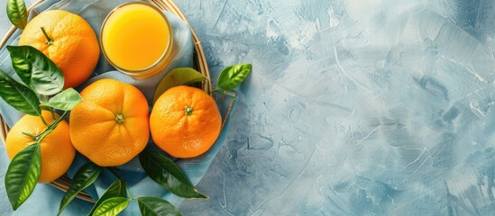 Canvas Print - Top down view of a basket containing oranges with leaves accompanied by a glass of orange juice set on a bright background with ample copy space image