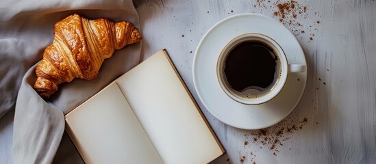 Sticker - Top view of a cup of coffee croissant and a white book on a table with additional copy space for images