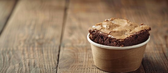 Poster - A brownie cake rests in a paper cup on a wooden table providing a backdrop for free text and advertising in the copy space image