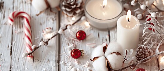 Fototapete - Close up top view of a festive arrangement featuring a cotton branch candles and a candy cane on a white wooden backdrop ideal for Christmas and New Year festivities with ample copy space image