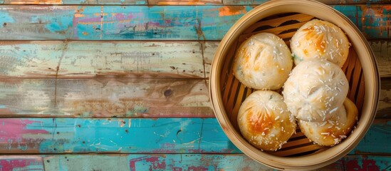 Canvas Print - A bamboo bowl filled with steamed bread topped with coconut jam is placed on a colorful wooden table providing a perfect copy space image from above