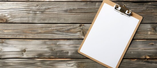 Fototapete - Top view of a clipboard with white paper on a wooden backdrop suitable for use as a mock up copy space image