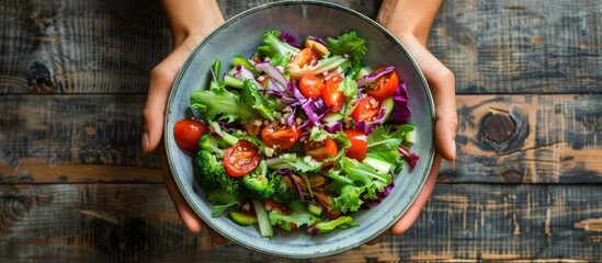 Aufkleber - Close up top view of a hand holding a mixed salad bowl on a wooden table with copy space image