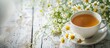 © HN Works - Close up of chamomile herbal tea in a cup on a white wooden table with a chamomile bouquet showcasing a copy space image for the natural healer concept and promoting herbal immunity tea
