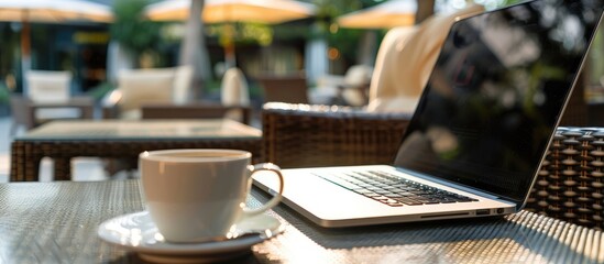 Poster - Close up view of an open laptop next to a coffee cup on a hotel terrace table representing technology business and modern lifestyle in a copy space image