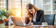 © Anhen Design - A young businesswoman sits at her desk, holding her head in frustration. She looks stressed and overwhelmed, with a laptop, coffee cup, and documents spread around her in a modern office setting.