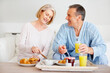 © STEEXBuyout/peopleimages.com - Mature couple, smile and breakfast together on sofa with bonding, diet nutrition and support in home. Happy, man and woman with morning meal, healthy food and romantic time for love relationship