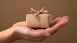 © sarana - Hand Holding a Gift Box: A hand holding a small gift box wrapped with a bow, suggesting a present or surprise.