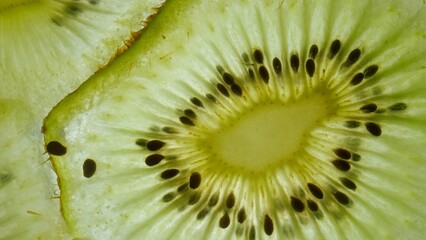 Macro shot of fresh juicy green kiwi slice against skylight, showing flesh and seeds with watery texture structure of fruit visible under light.