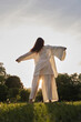 © yavdat - A person in flowing white garments extends their arms in a wide gesture against a sunset backdrop. The photo highlights the sense of liberation and harmony with the natural world.