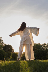 a person in flowing white garments extends their arms in a wide gesture against a sunset backdrop. t