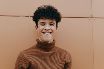 Wall Mural - Fashionable young man smiling in brown turtleneck sweater, standing in front of orange wall