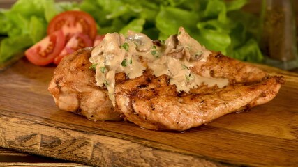 Wall Mural - Grilled chicken breast, topped with creamy mushroom sauce, served on a wooden plate with vegetables. Movement from left to right