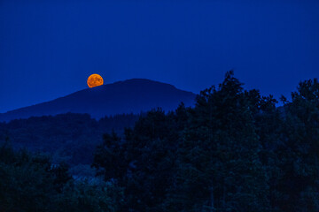 The full flower moon -  07, 2024. The rising moon over the mountain peaks , a cloudless night allows observation of the astronomical phenomenon. 