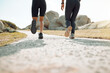 © peopleimages.com - Running, people and legs or fitness on road for wellness, health and exercise by beach. Athlete, cardio and personal trainer or together in morning for outdoor workout and sport or friends in nature