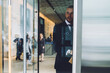 © BullRun - Experienced owner of financial company dressed in formal wear going out on street from modern office building on coffee break.Young businessman standing on entrance and opening glass door