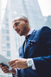 © BullRun - Side bellow view of confident experienced entrepreneur dressed in formal wear searching information on website on modern touch pad using 4G internet in modern business city with high skyscrapers