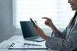 © Wasana - A woman is sitting at a desk with a laptop and a cell phone
