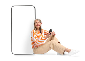 Poster - Happy mature woman holding mobile phone and sitting near big smartphone on white background