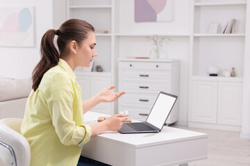 Canvas Print - Sick woman with pills having online consultation with doctor via laptop at white table indoors