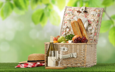 Canvas Print - Picnic basket with foods and wine on green grass outdoors. Space for text