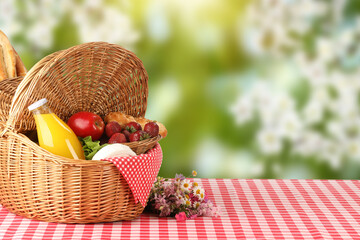 Poster - Picnic basket with foods and juice on table in nature. Space for text