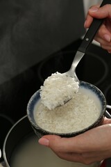 Wall Mural - Woman taking boiled rice from pot into bowl, closeup