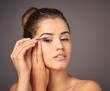 © AK Coop/peopleimages.com - Mascara, cosmetics and face of woman in studio for wellness, beauty and makeup on gray background. Cosmetology, salon aesthetic and girl with eyelash brush for application, lash tools and glamour