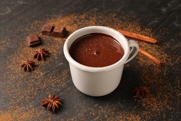 Wall Mural - Tasty melted chocolate in cup and spices on dark textured table, closeup