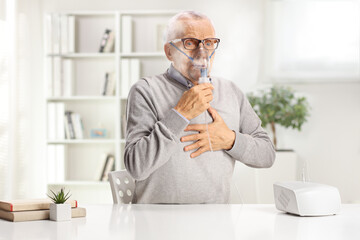 Wall Mural - Elderly man with breathing problem sitting at a table and using a nebulizer