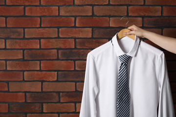 Wall Mural - Woman holding hanger with shirt and necktie near red brick wall, space for text