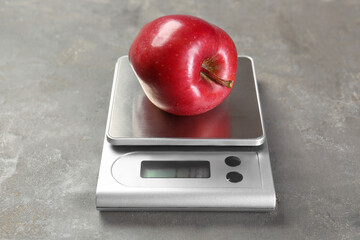 Wall Mural - Kitchen scale with apple on grey textured table, closeup