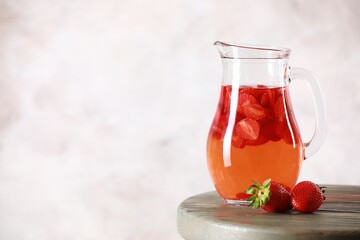 Canvas Print - Tasty strawberry lemonade in jug and berries on wooden table against light background. Space for text