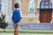 © Dragana Gordic - A young Caucasian boy stands outside with a bright blue backpack, looking at the school entrance, anticipation for a day of learning evident in his stance.