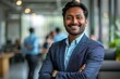 © Rising Monk - portrait of a handsome smiling asian indian businessman boss in a suit standing in his modern business company office. his workers standing in the blurry background. Generative AI