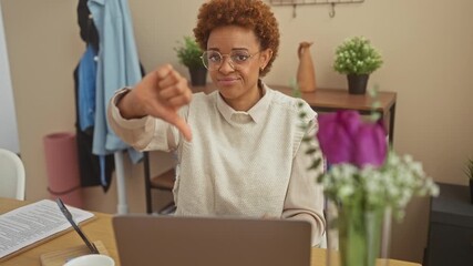 Sticker - Unhappy african american woman at home, sitting at table showing negative thumb down gesture. angry, looking down with a bad expression.