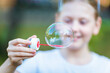 © jane_moss - A little girl blows a huge soap bubble in the park in the summer. Blurred portrait with bokeh.