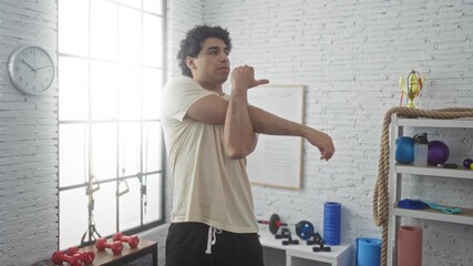 Sticker - A handsome young man stretches his arms in an indoor gym filled with equipment, showcasing fitness and determination.