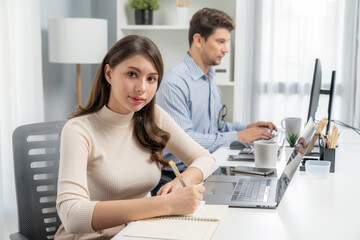 Wall Mural - Smiling beautiful woman taking crucial note on paperwork, looking at camera photo shooting portrait business pose profile while working with smart coworker at modern office at morning time. Postulate.