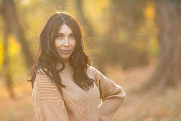 Attractive stylish woman walking in park, dressed in warm brown suit. Pretty woman with brunette hair. Smiling girl on a background of golden leaves. Autumn fashion accessories in street fashion style