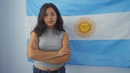 Wall Mural - Young woman standing indoors in front of an argentinian flag, posing for a photo with a confident expression.