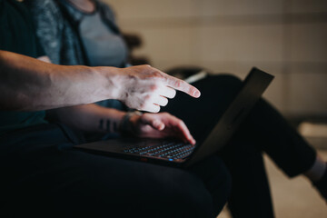 Canvas Print - Close-up of a person's hand pointing at a laptop screen during a business discussion outdoors at night.