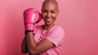 © britaseifert - Bald beautiful woman wearing pink shirt and smiling with a boxing glove above on pink background