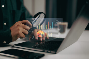 Fototapete - Person using a magnifying glass to examine data visualizations on a laptop. It represents the importance of detailed analysis and scrutiny in data-driven decision-making processes
