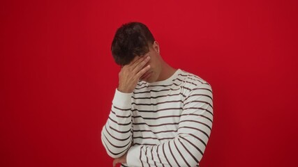 Canvas Print - Young hispanic man wearing stripes t shirt standing serious with eyes covering hand, concept of sadness and rejection over isolated red background