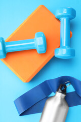 Poster - Two dumbbells, yoga block, fitness elastic band and thermo bottle on light blue background, flat lay