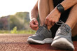 © New Africa - Man tying shoelace of grey sneaker at stadium, closeup. Space for text